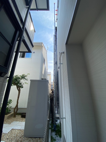 壁面とフェンスの間に限られた空間がある現場。建物同士の間隔や設備の配置を見て、施工方法を検討します。