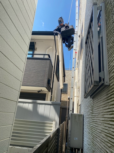 住宅の狭所でロープと高所作業技術を使用してエアコン工事を行う職人