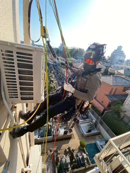 高所の外壁でロープアクセスを使用して室外機のエアコン工事を行う職人