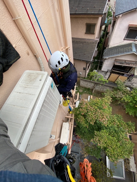 壁面の室外機のすぐ横で作業する職人