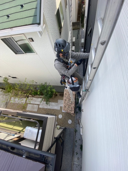 狭い建物間で、外壁の施工箇所へ体を近づけている職人
