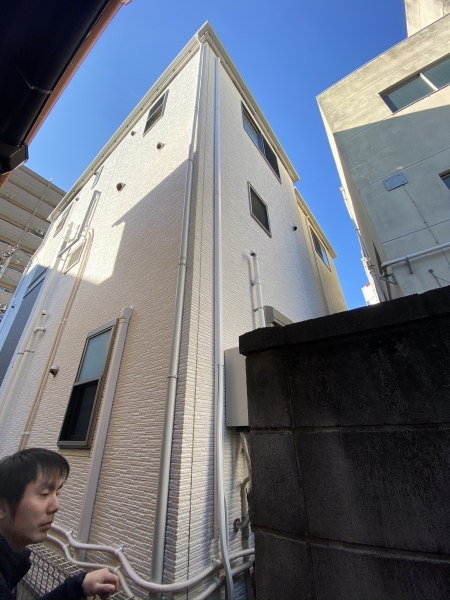 新築3階建て住宅の建物側面と敷地境界を確認するクアトロテクノサービスの職人