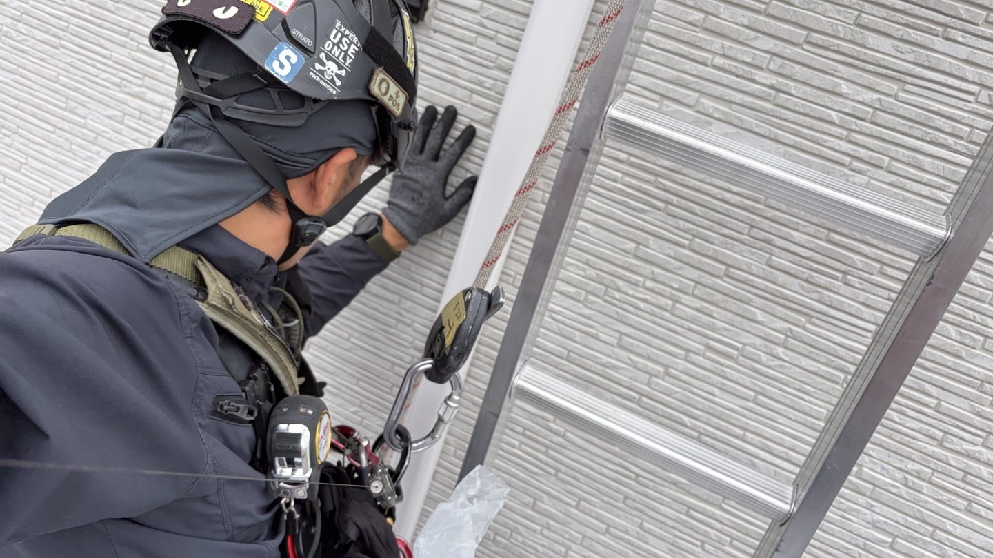 狭い建物間で、外壁の施工箇所へ体を近づけている職人