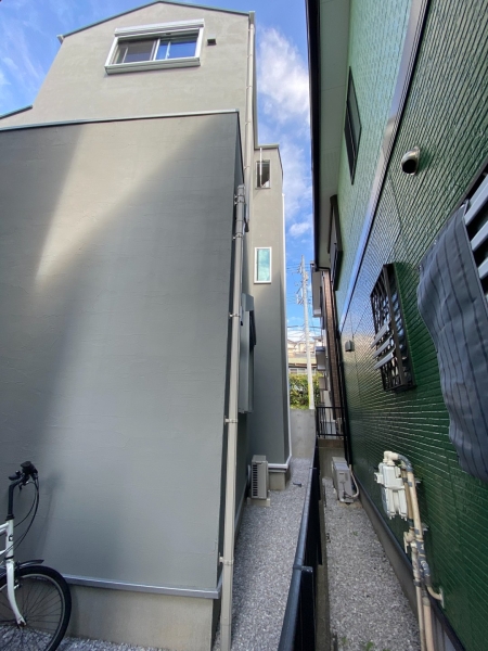 作業前に建物を横から撮影した写真です。建物間の通路や外壁まわりなど、施工前の現場の様子を示しています。