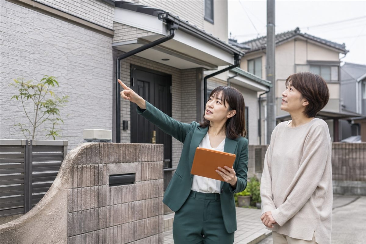 住宅の外壁や建物状態を確認する査定担当者と所有者